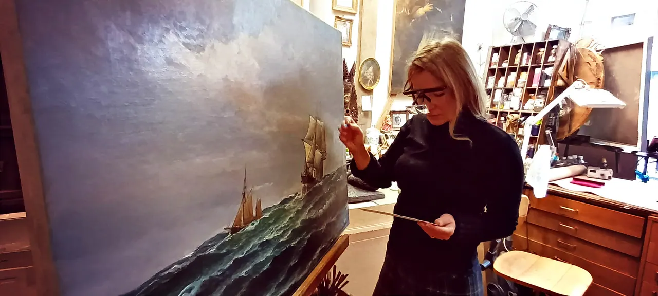 Isabelle Pitre, maître restaurateur de tableaux à Paris, examinant à la lampe-loupe une grande marine ancienne sur chevalet dans son atelier du 28 rue Traversière